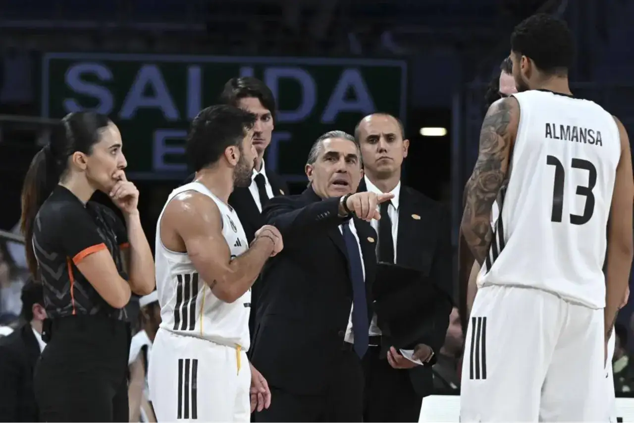 Entrenador del r madrid baloncesto señala una jugada. Jugadores y árbitra observan.