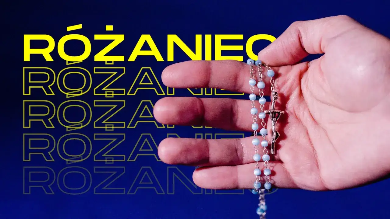 Dłoń trzymająca różaniec z niebieskimi paciorkami i krzyżem.