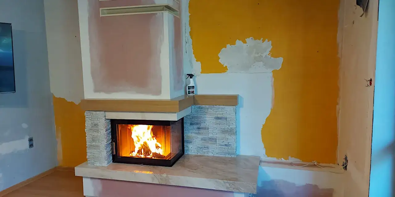 Nowa obudowa do kominka z kamienia i drewna, z palącym się ogniem. Wnętrze w trakcie remontu.