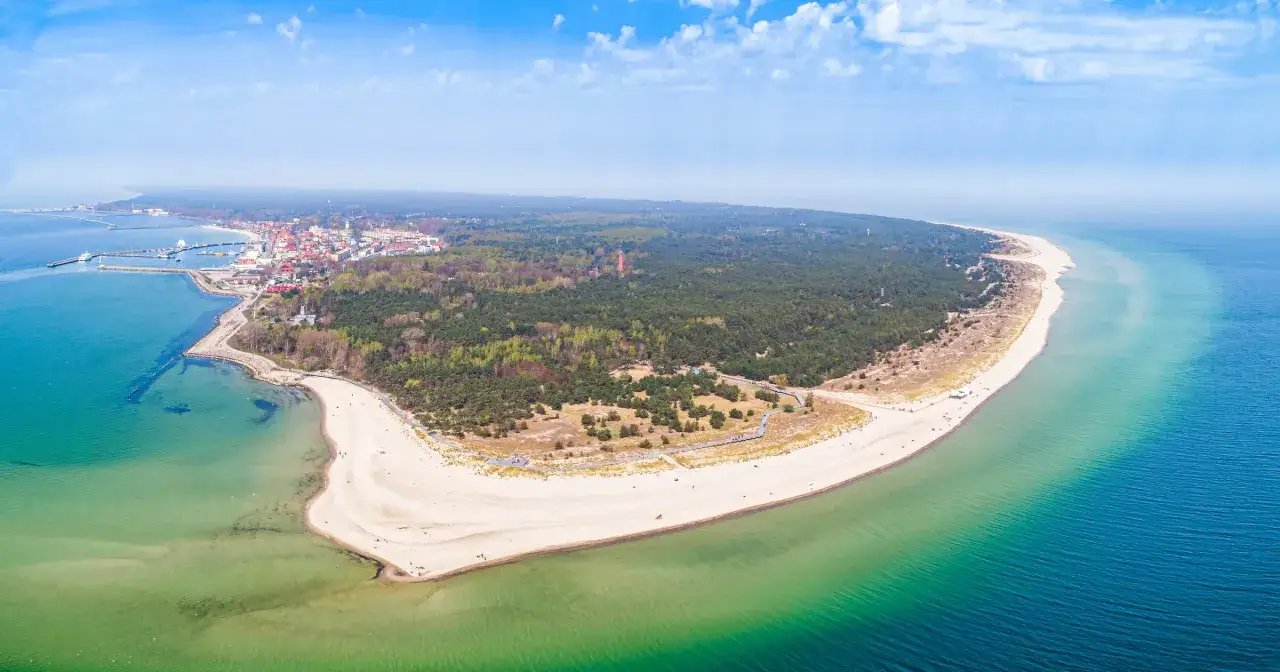 Malownicze wybrzeże pomorza gdańskiego z piaszczystą plażą, lasem sosnowym i miasteczkiem nad zatoką.