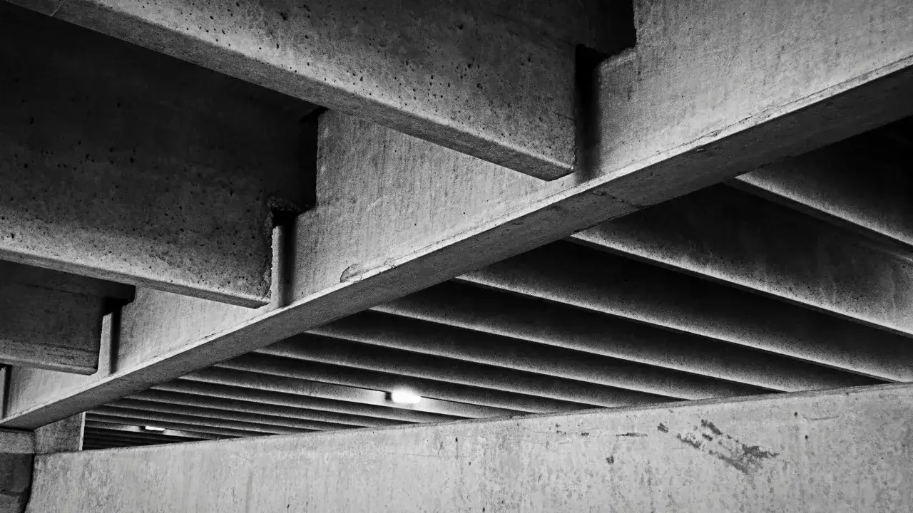 Podziemny parking z betonowymi belkami i żebrowanym sufitem. Klasy betonu b tworzą surową, geometryczną przestrzeń.