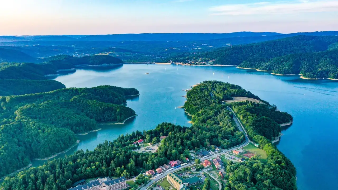 Widok z lotu ptaka na jezioro otoczone lasami, z widocznymi zabudowaniami i zaporą.