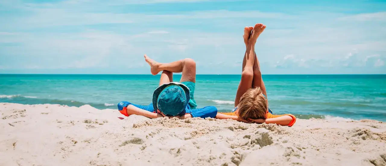 Dzieci leżą na plaży, marząc o wakacjach. Szukając noclegów nad morzem, warto pomyśleć o takich beztroskich chwilach.