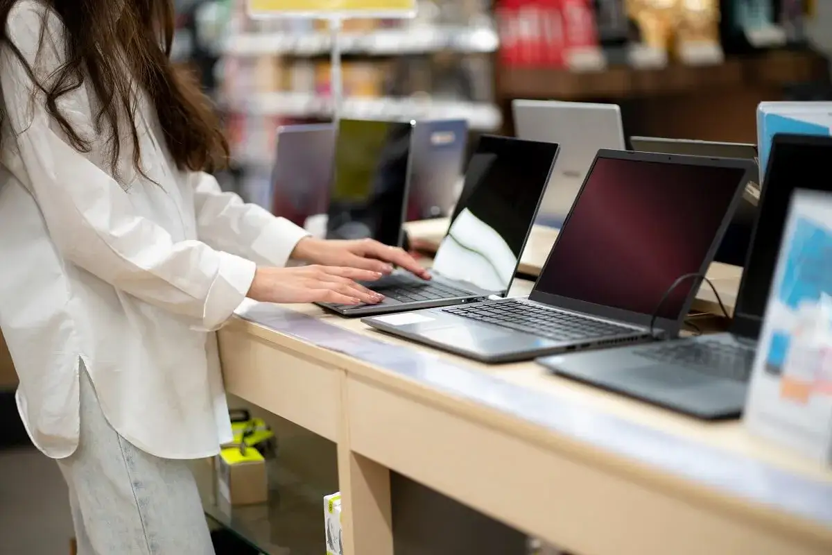 Kobieta w białej koszuli testuje laptopy na wystawie sklepowej.