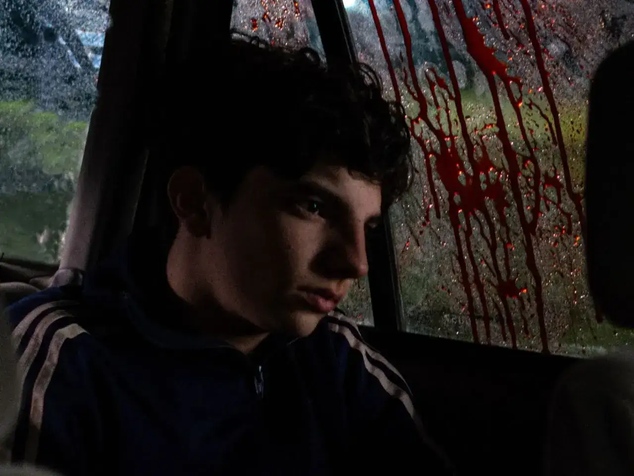 Młody chłopak w samochodzie, patrzący na ślady krwi na szybie. Czuć, gdy rodzi się zło.