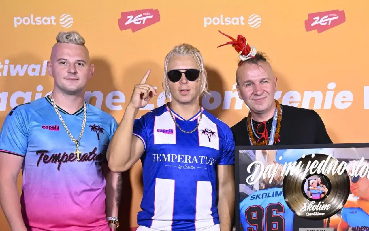 Trzech mężczyzn pozuje do zdjęcia. Jeden z nich trzyma złotą płytę.