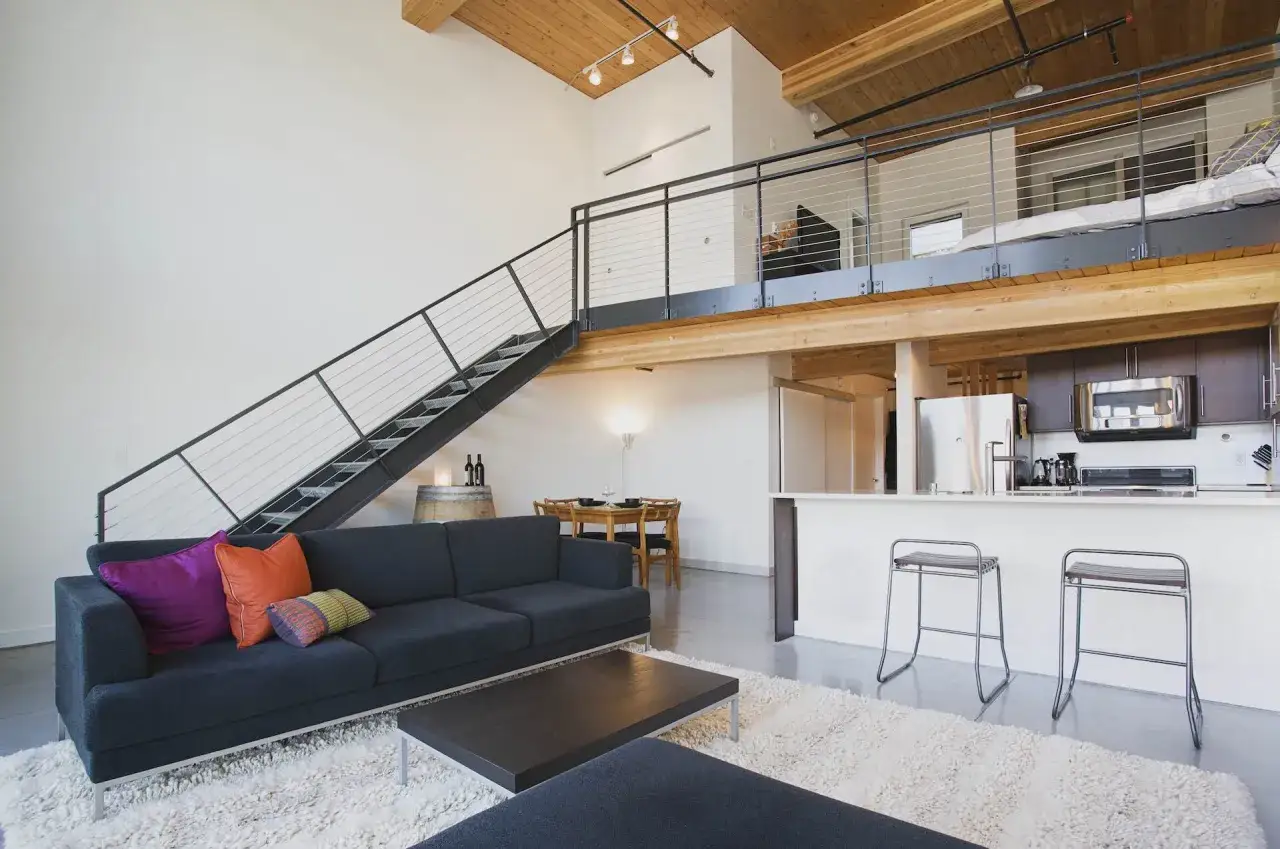 Nowoczesne mieszkanie z antresolą, co to jest? Widoczna otwarta przestrzeń z kanapą, schodami na piętro i aneksem kuchennym.