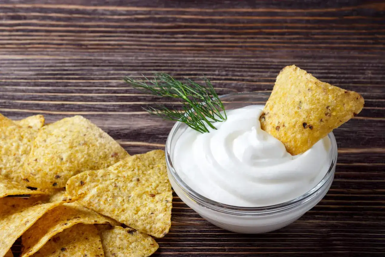 Nachos z gęstym, białym sosem śmietanowym i gałązką koperku na drewnianym tle.