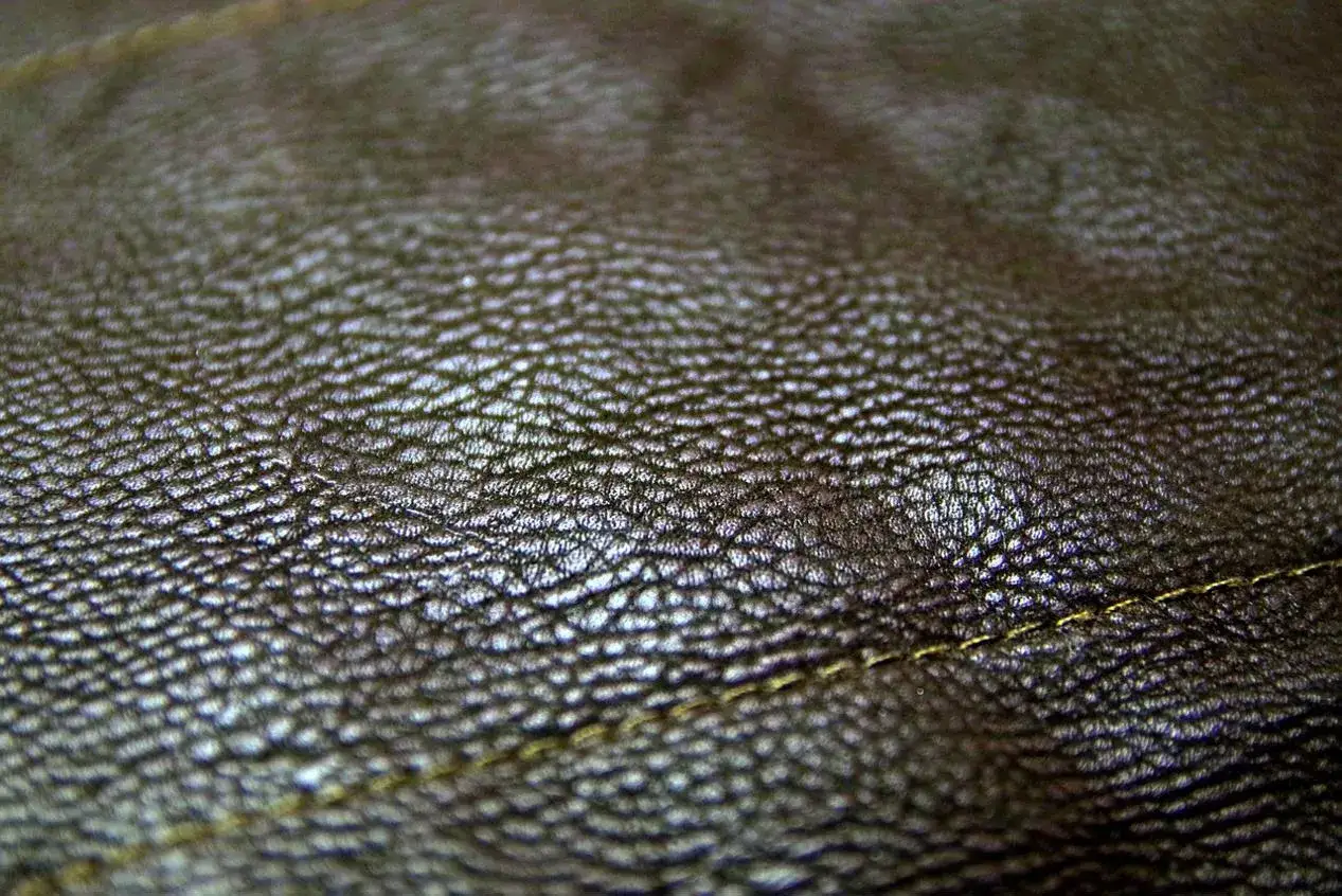 Zbliżenie na fakturę ciemnobrązowej skóry. Real leather to naturalny, trwały materiał, który pięknie się starzeje. Widoczny delikatny szew.