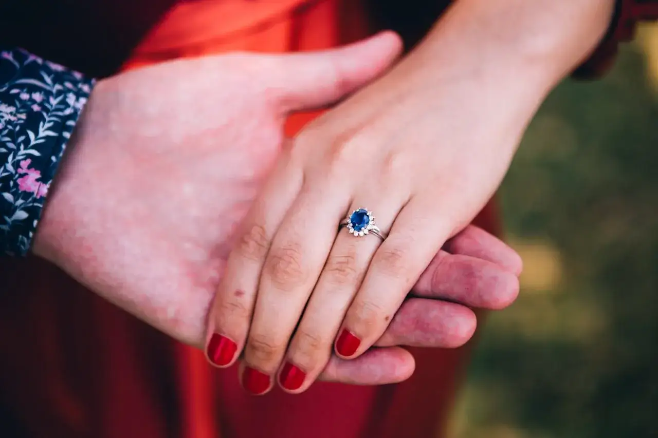 Dłoń z pierścionkiem z dużym szafirem, otoczonym białymi kamieniami. Czy to szafir czy szmaragd?