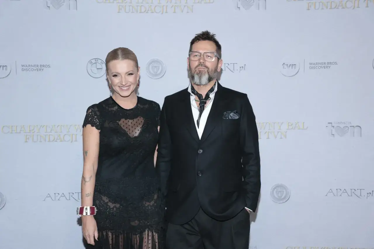 Michał Cessanis żona, ubrana w koronkową sukienkę, pozuje obok męża w eleganckim garniturze.