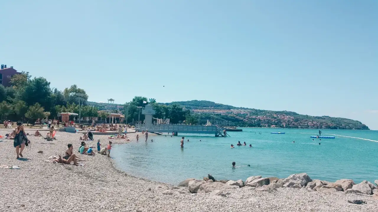 Plaża w Słowenii, ludzie kąpią się w morzu. Odpowiedź na pytanie: czy Słowenia ma dostęp do morza? Tak, ma!