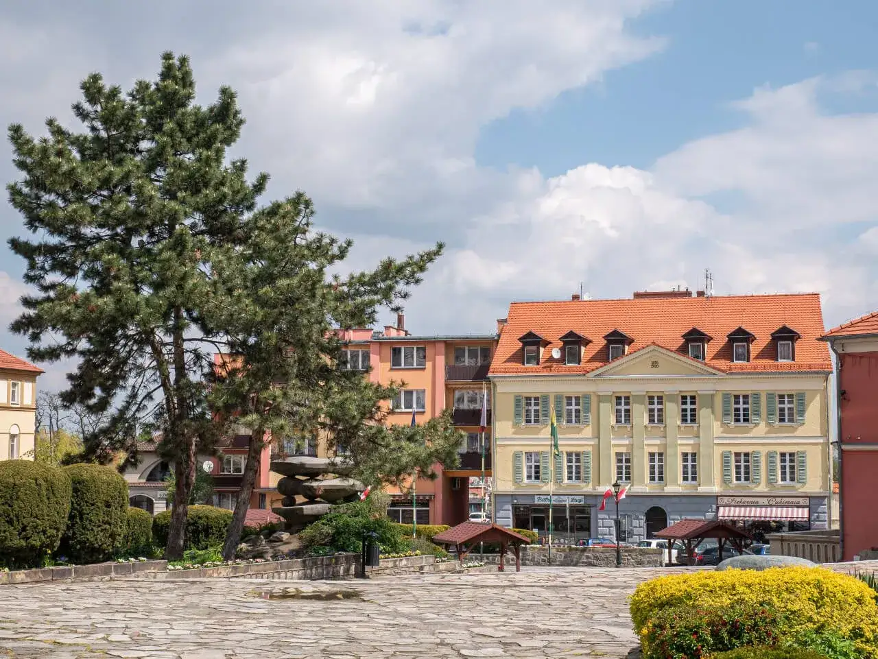 Rynek w Sobótce z kamienną rzeźbą i żółtym budynkiem.