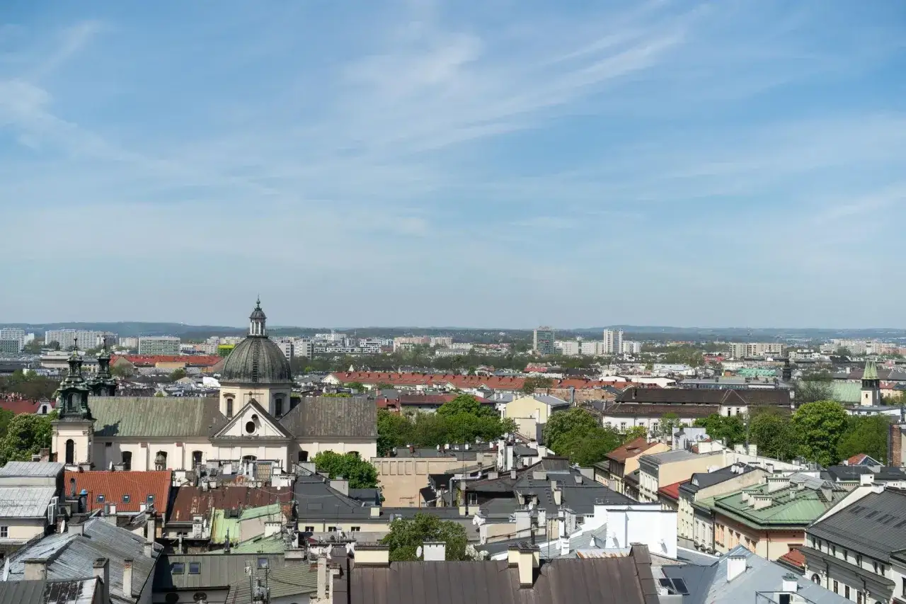 Widok na krakowskie dachy i kościół z kopułą. W tle nowoczesne budynki, które mogą wpływać na ceny mieszkań w Krakowie za m2.