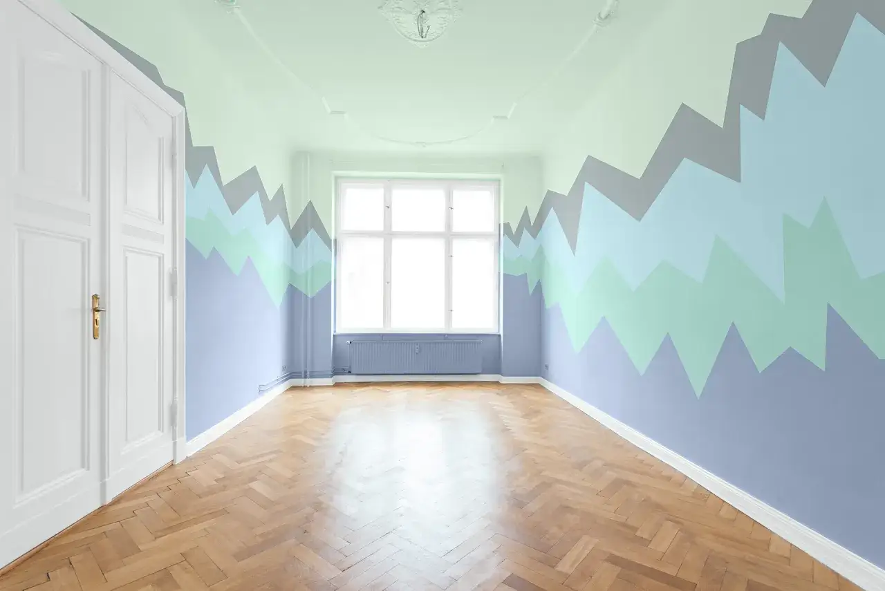 Pokój z falującym wzorem na ścianach w odcieniach niebieskiego i zieleni. Czy malować sufit w kolorze ścian? Jasny sufit i białe drzwi kontrastują z kolorowymi ścianami.