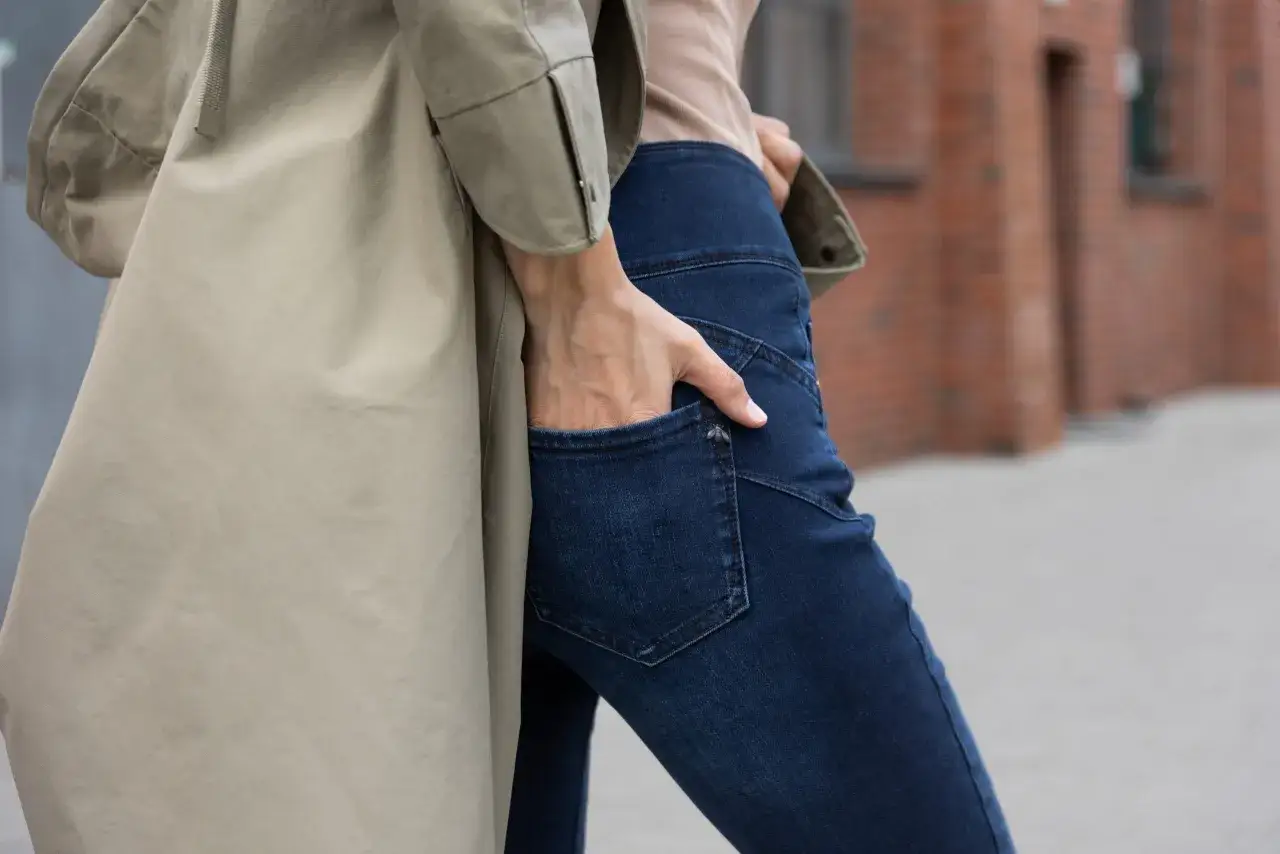 Kobieta w beżowym płaszczu i granatowych jeansach bootcut, które delikatnie rozszerzają się ku dołowi.