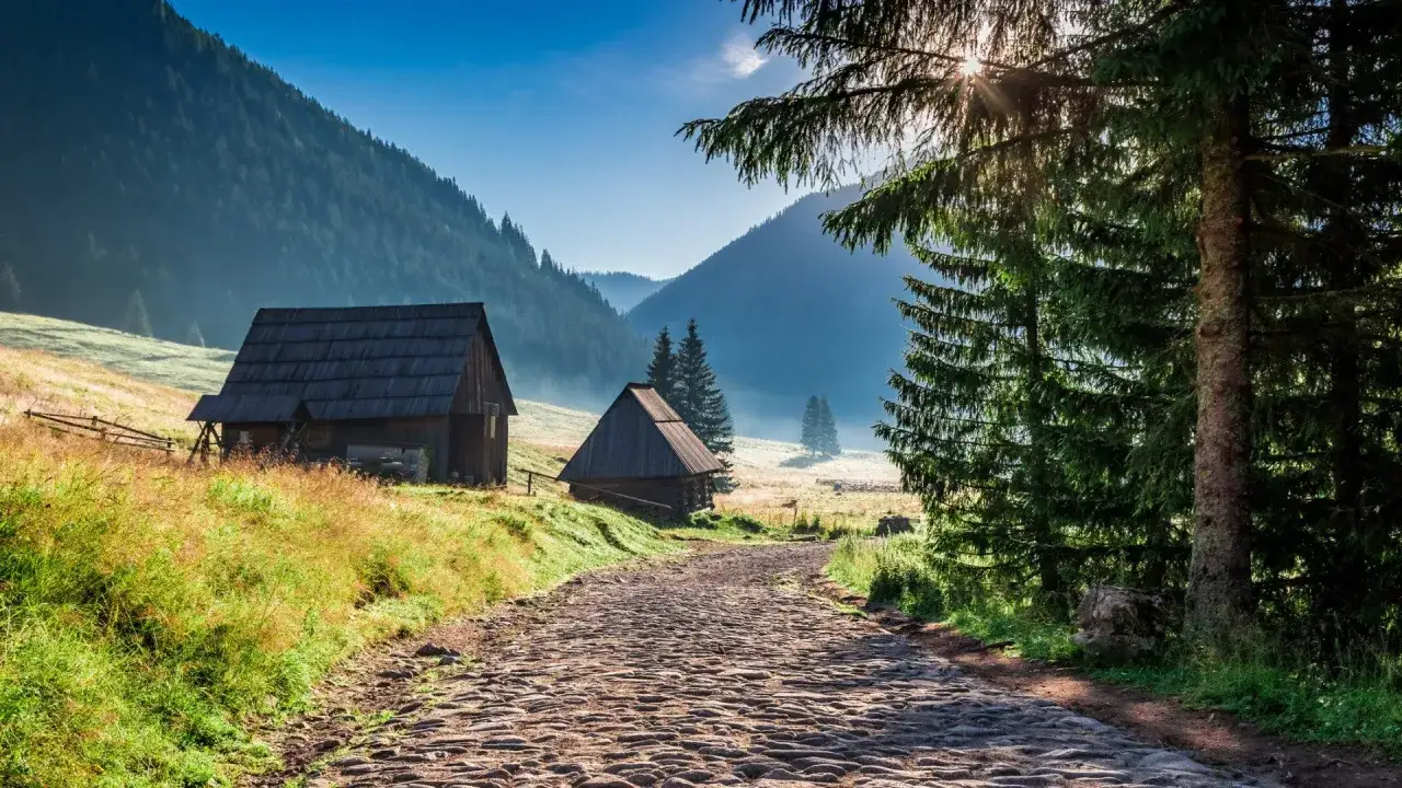 Kamienna droga prowadzi do bacówki w Dolinie Chochołowskiej. Drewniane chaty toną w porannej mgle, otoczone zielenią i majestatycznymi szczytami Tatr.