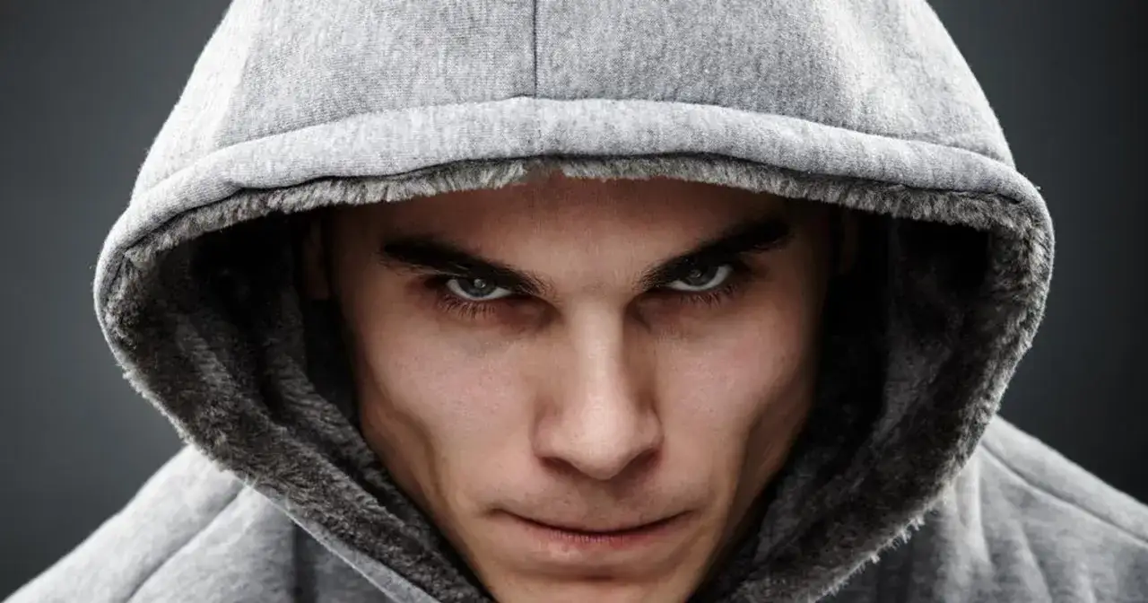 Mężczyzna w szarym kapturze, patrzący intensywnie w obiektyw.