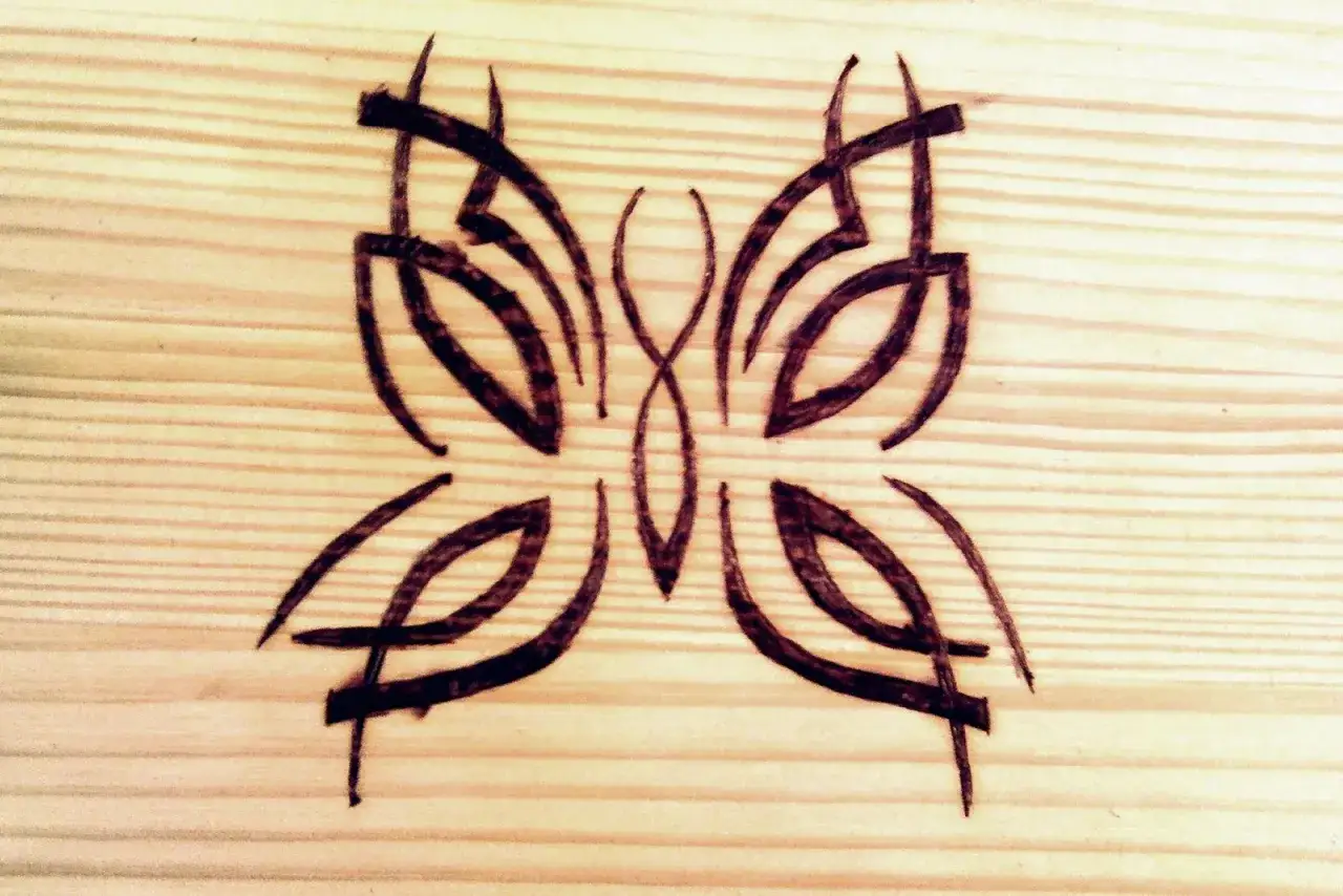 Stylizowane wzory do wypalania w drewnie, przypominające motyla.