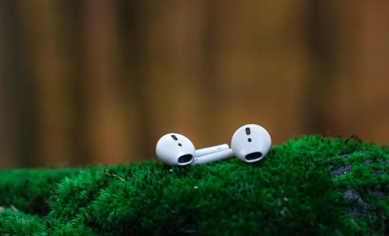 Białe słuchawki AirPods leżące na zielonym mchu.