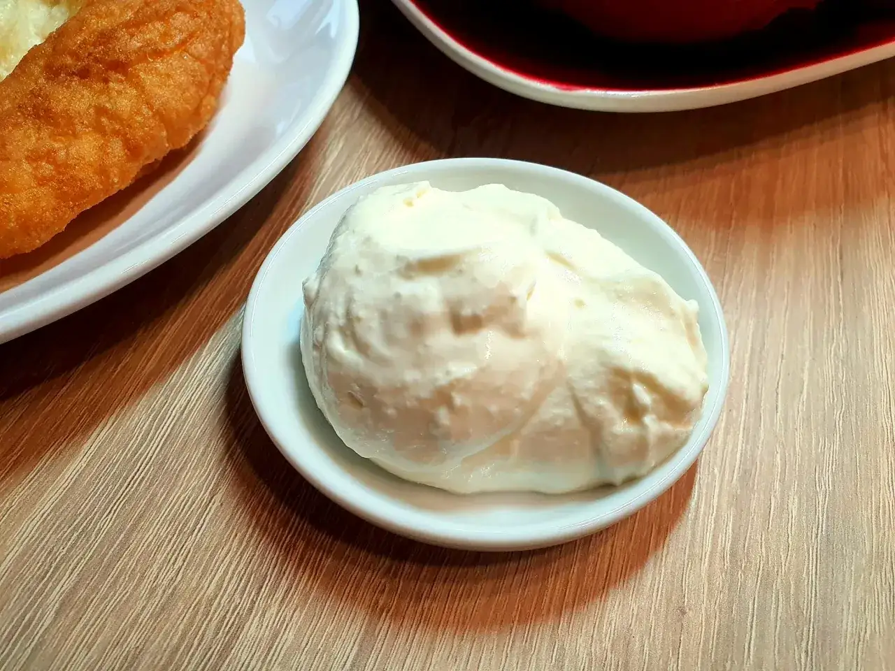 Kremowy, puszysty kajmak bałkański w białej miseczce, gotowy do podania z chrupiącym plackiem.