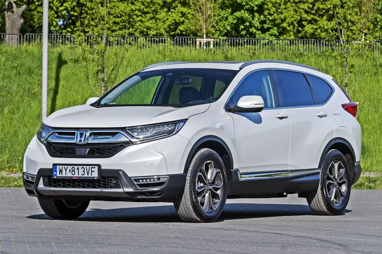 Biała Honda CR-V zaparkowana na zewnątrz, z zielenią w tle.