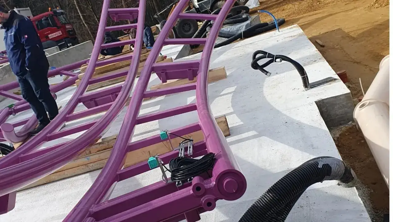 Lila Achterbahnteile im Bau, ein Mann steht darauf.