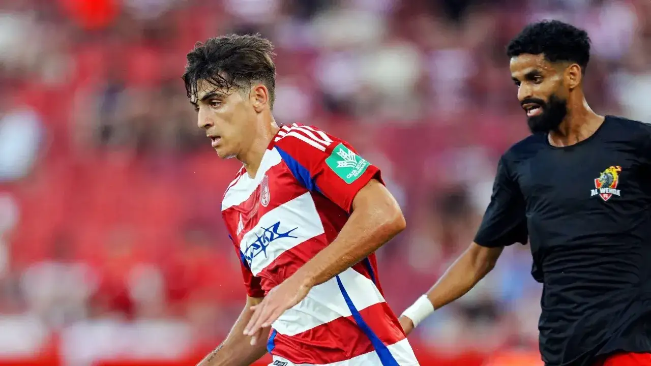 Jugadores de fútbol en acción, uno con camiseta a rayas rojas y blancas, otro con camiseta negra.
