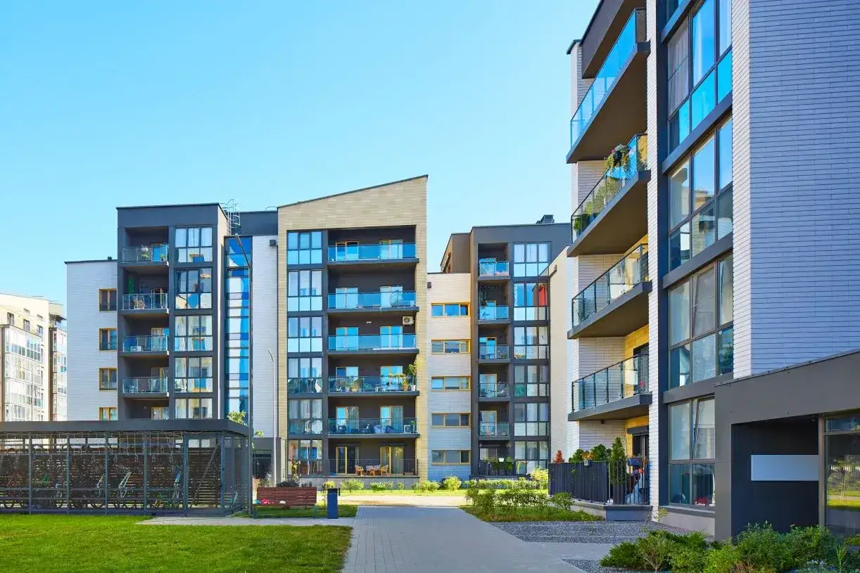 Nowoczesne bloki mieszkalne z balkonami i zielonym terenem przed nimi.