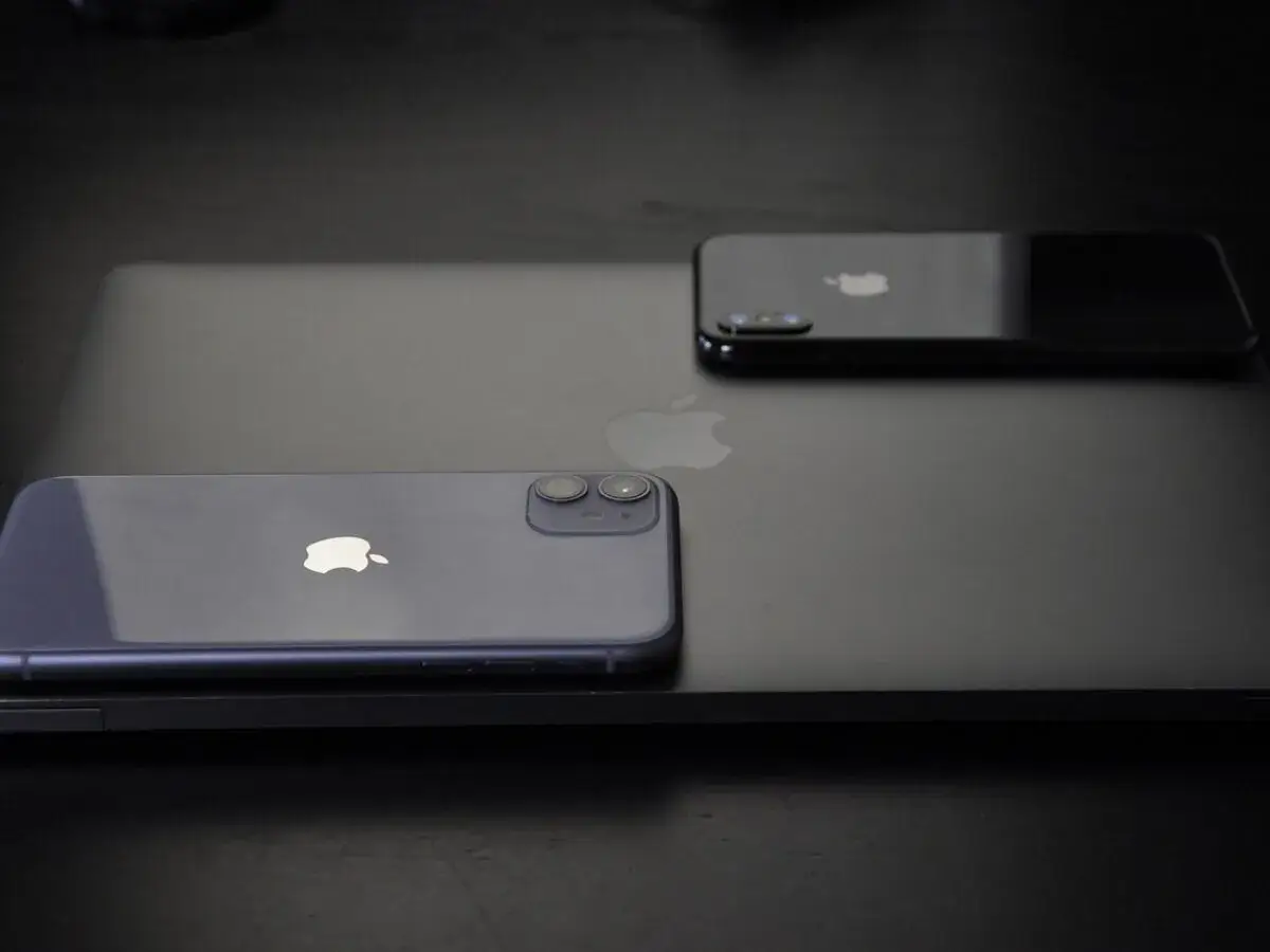 Dwa iPhone'y, w tym jeden fioletowy, leżą na czarnym laptopie. Zastanawiasz się, jak wyłączyć iPhone'a 11?