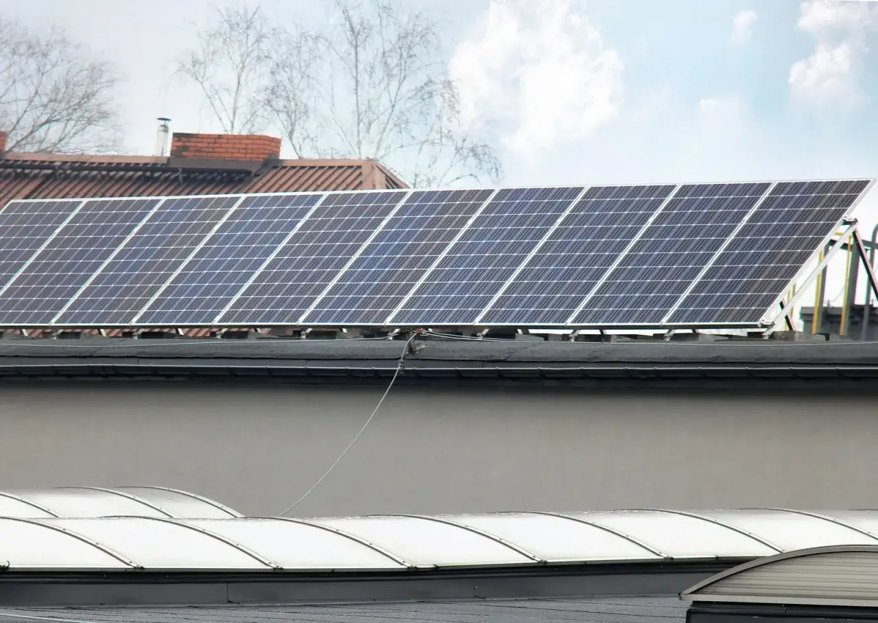 Panele fotowoltaiczne na dachu, gotowe do podgrzewania i produkcji energii. W tle budynki i drzewa.