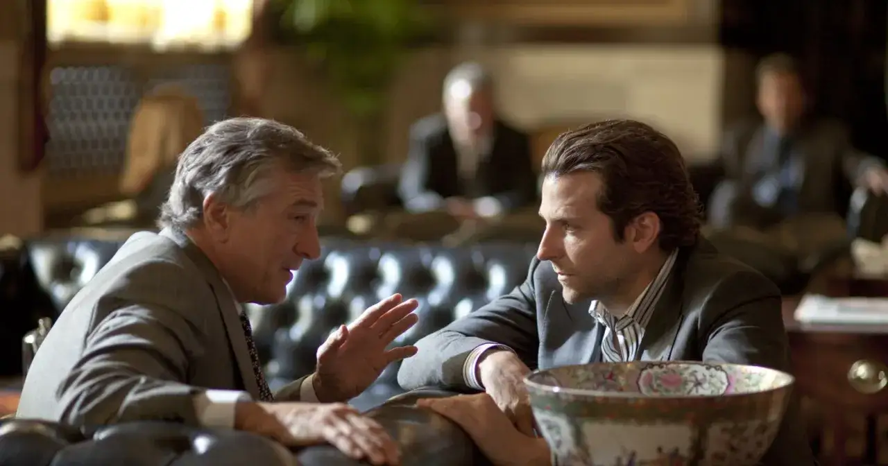 Dwóch mężczyzn w garniturach rozmawia, jeden gestykuluje. Scena z filmu "Jestem bogiem".