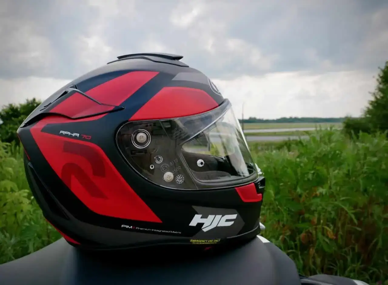 Czerwono-czarny kask motocyklowy HJC RPHA 70 z przyciemnianą blendą, gotowy na podróż pośród zieleni.