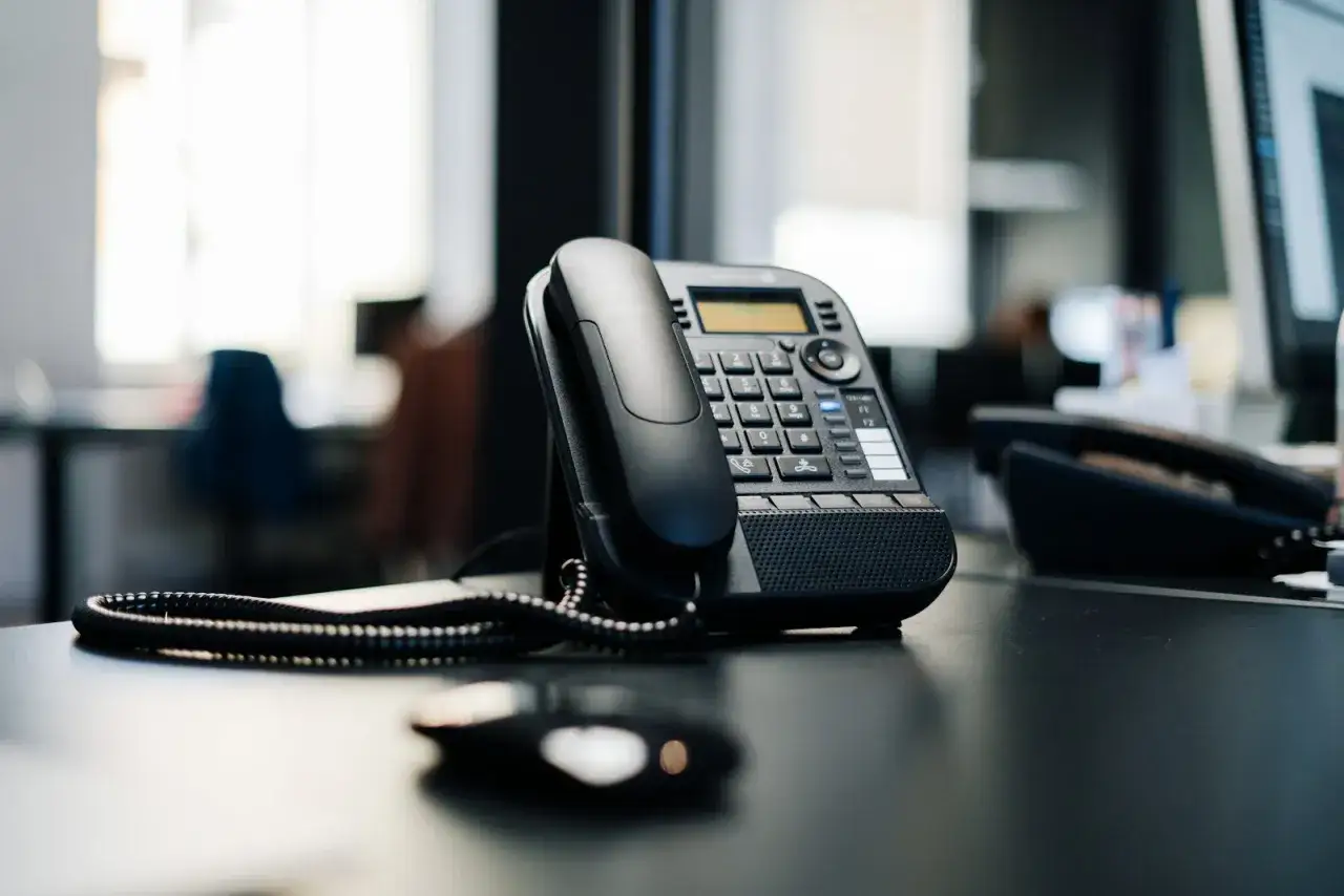 Czarny telefon biurowy na biurku. Słychać dzwonek, jakby numer zablokowany dzwonił, ale nikt nie odbiera.