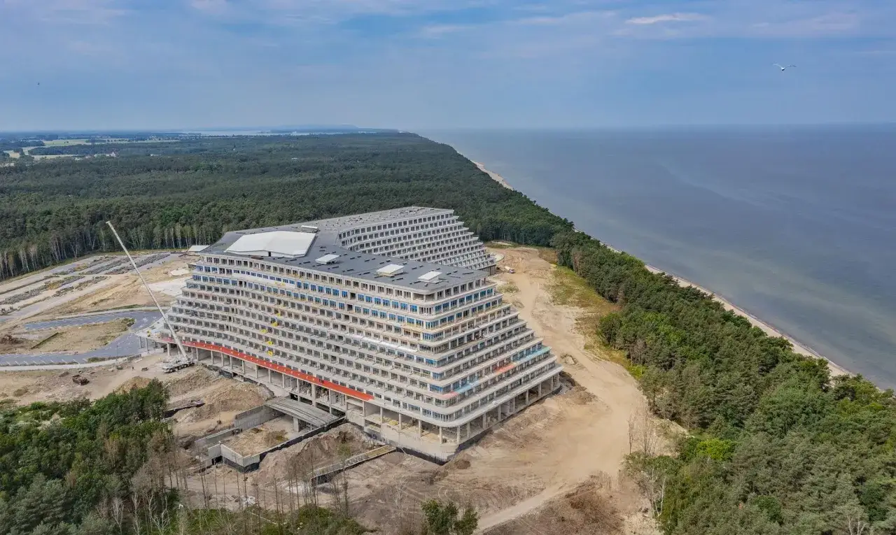 Ogromny hotel w kształcie tarasów w budowie, nad morzem, otoczony lasem.