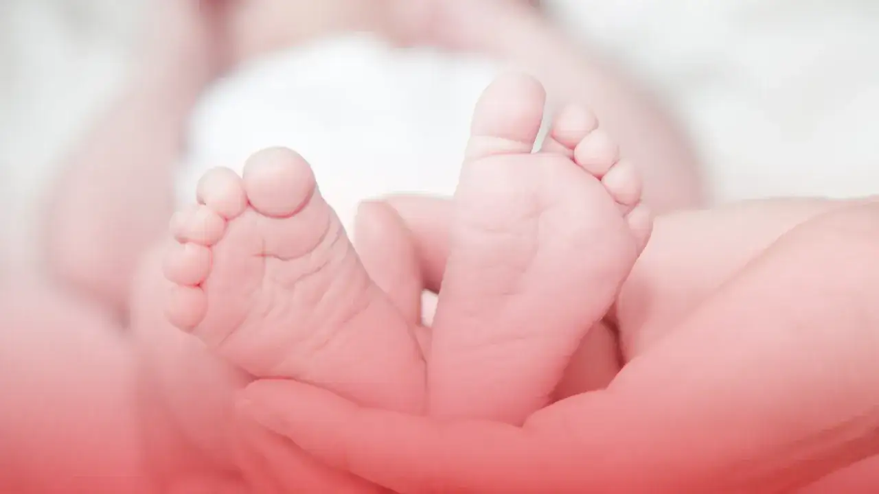 Dłonie trzymające stopy noworodka.