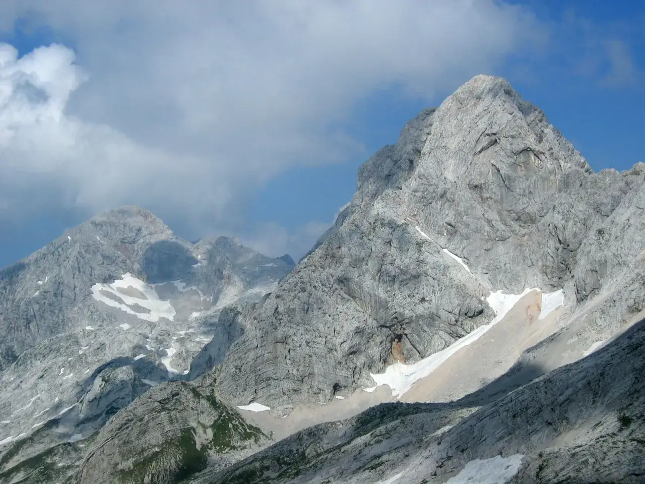Majestatyczne szczyty Alp Kamnickich, skaliste zbocza i resztki śniegu pod błękitnym niebem.