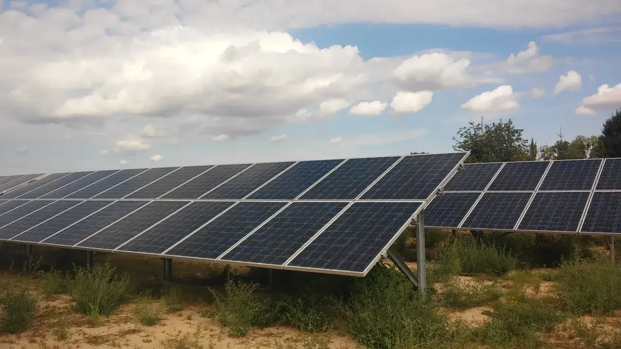 Rzędy paneli fotowoltaicznych na tle błękitnego nieba z chmurami. Firma oferuje sprzedaż energii z fotowoltaiki.