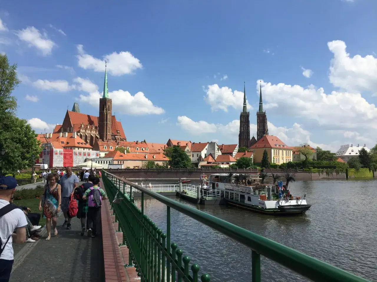 Mosty i katedra to to, z czego słynie Wrocław. Ludzie spacerują po moście, podziwiając widok na rzekę i zabytkową architekturę.