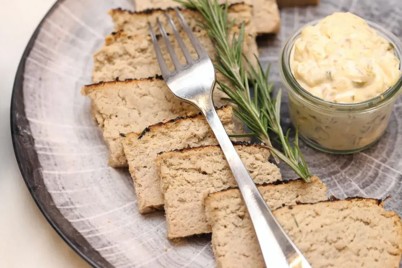 Pokrojony pasztet na talerzu z widelcem, gałązką rozmarynu i słoiczkiem sosu.