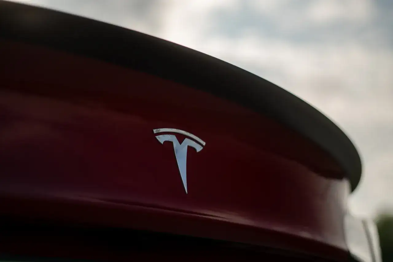 Chromowane logo Tesli na czerwonym samochodzie. Tesla, choć założona w USA, ma korzenie w Serbii, kraju wynalazcy Nikoli Tesli.