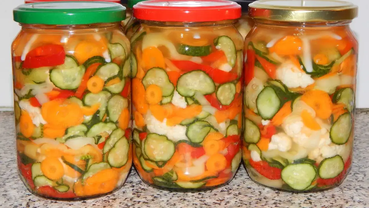 Trzy słoiki z marynowanymi warzywami: ogórkami, marchewką, papryką i kalafiorem.