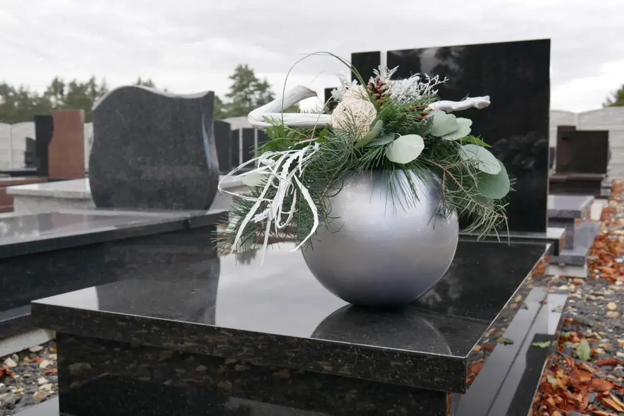Srebrna doniczka z zimową dekoracją na nagrobku, wśród innych pomników.