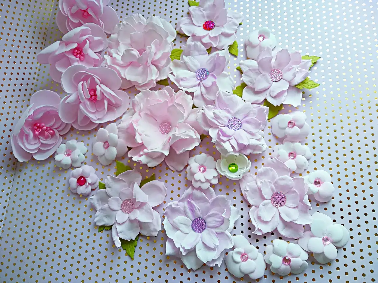Kwiaty z pianki dekoracyjnej jak zrobić: delikatne, różowe kwiaty z pianki z błyszczącymi środkami, ułożone na tle w złote kropki.