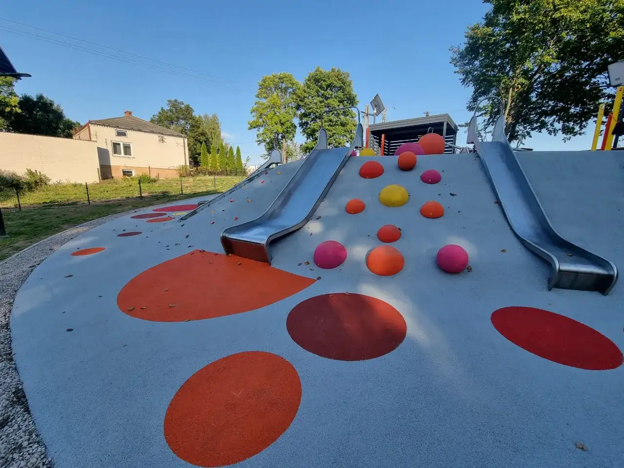 Plac zabaw z dwoma zjeżdżalniami i kolorowymi elementami na bezpiecznym podłożu.