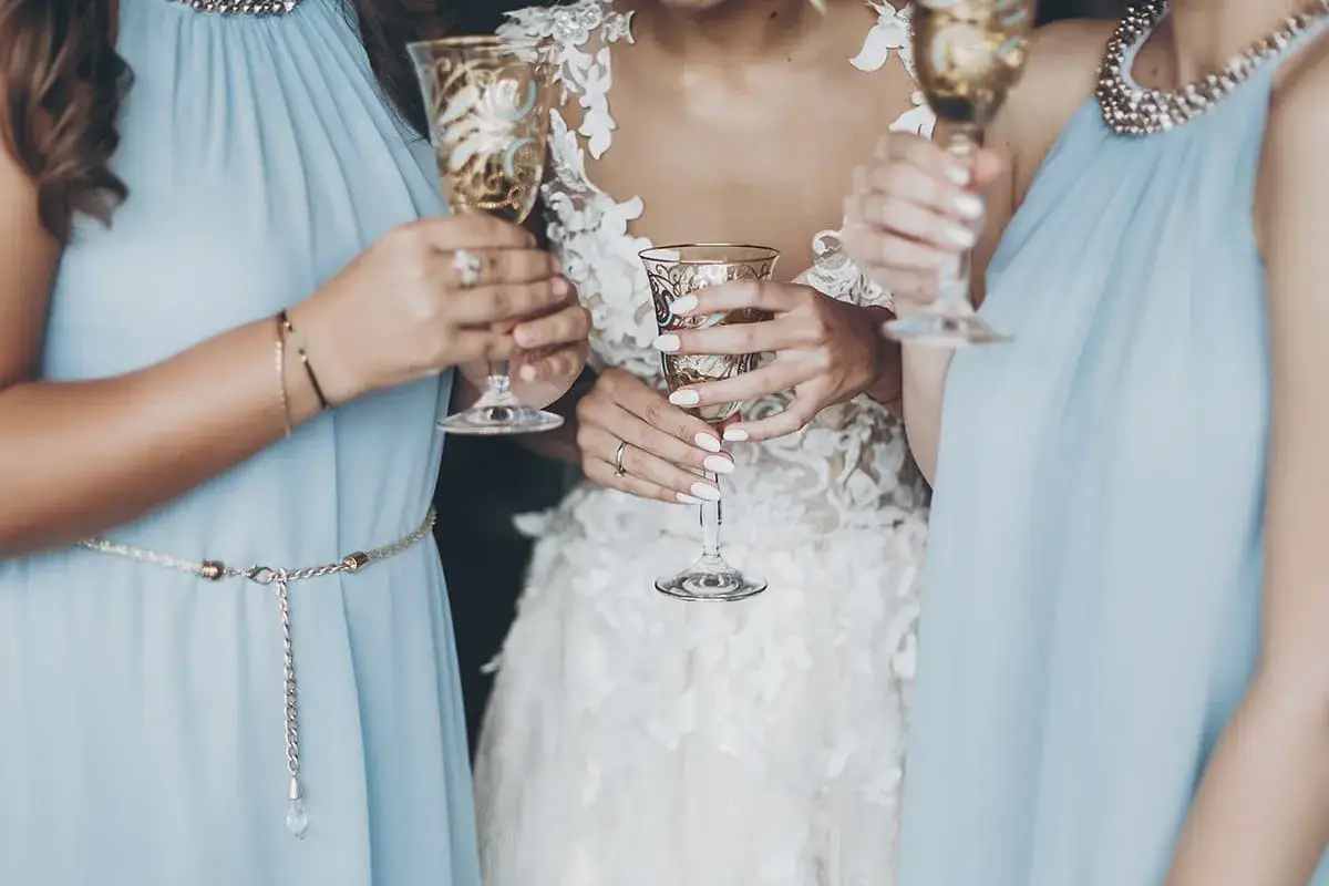 Panna młoda i druhny w błękitnych sukniach wznoszą kieliszki do toastu.