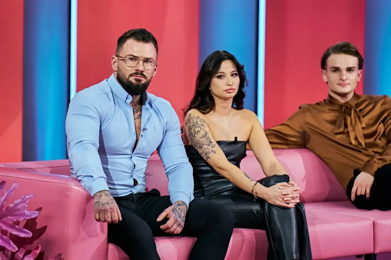 Uczestnicy "Love Never Lies Polska" siedzą na różowej kanapie. Mężczyzna w niebieskiej koszuli i kobieta w czarnym topie mają tatuaże.