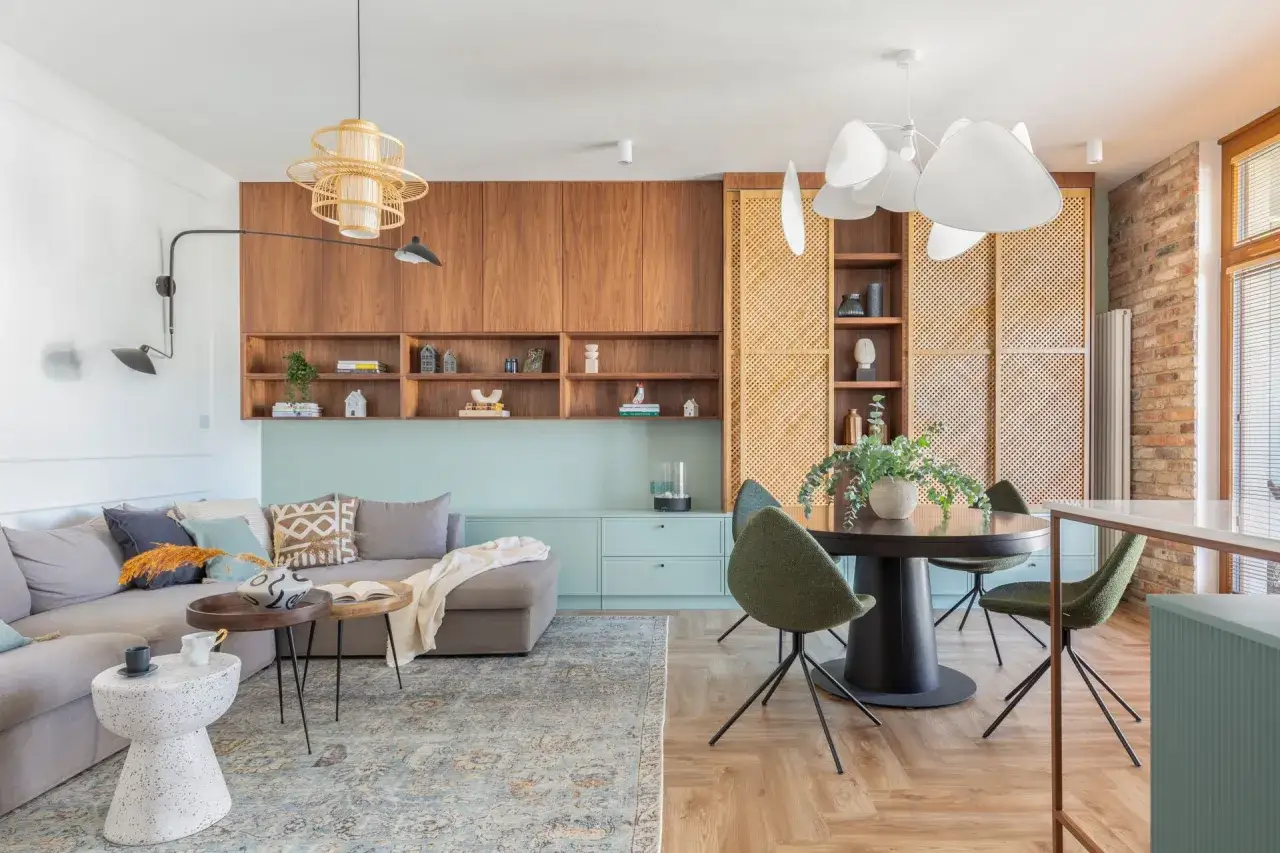 Przytulny, mały pokój w stylu boho z szarą kanapą, drewnianymi meblami i plecionymi elementami.