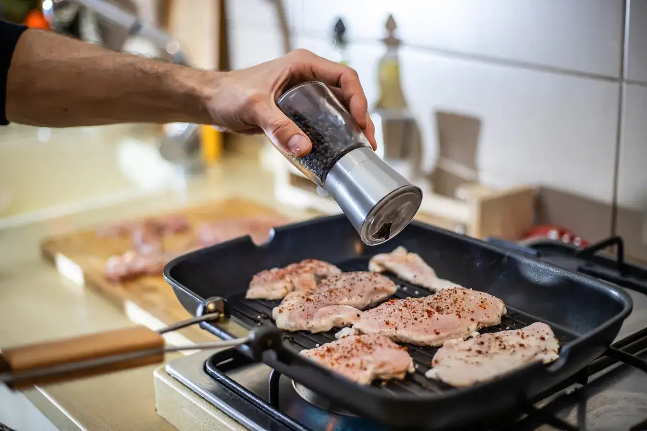 Doprawianie piersi kurczaka pieprzem przed smażeniem. Kluczowe jest, jak długo smażyć pierś z kurczaka, by była soczysta.