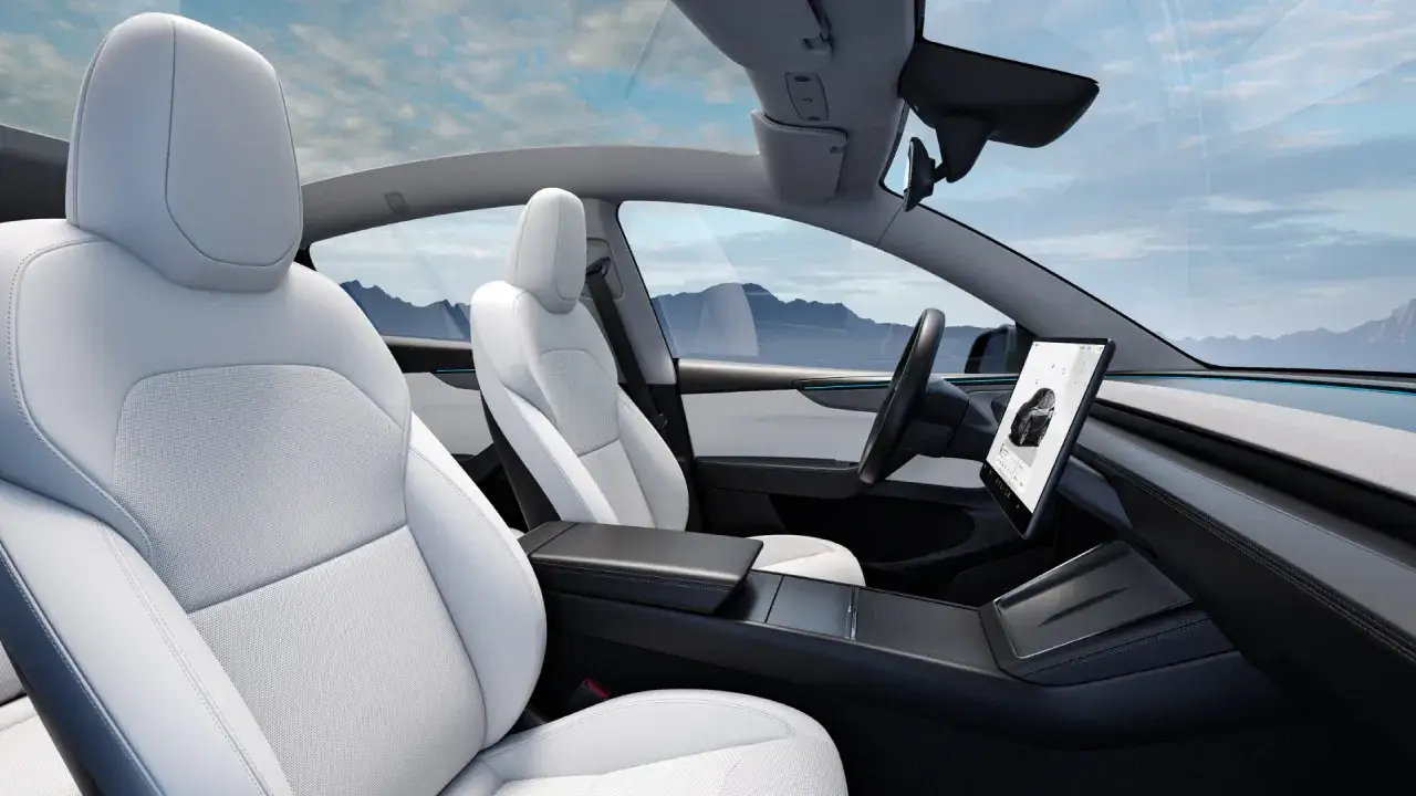 Wnętrze samochodu Tesla z białymi skórzanymi fotelami i dużym ekranem dotykowym.